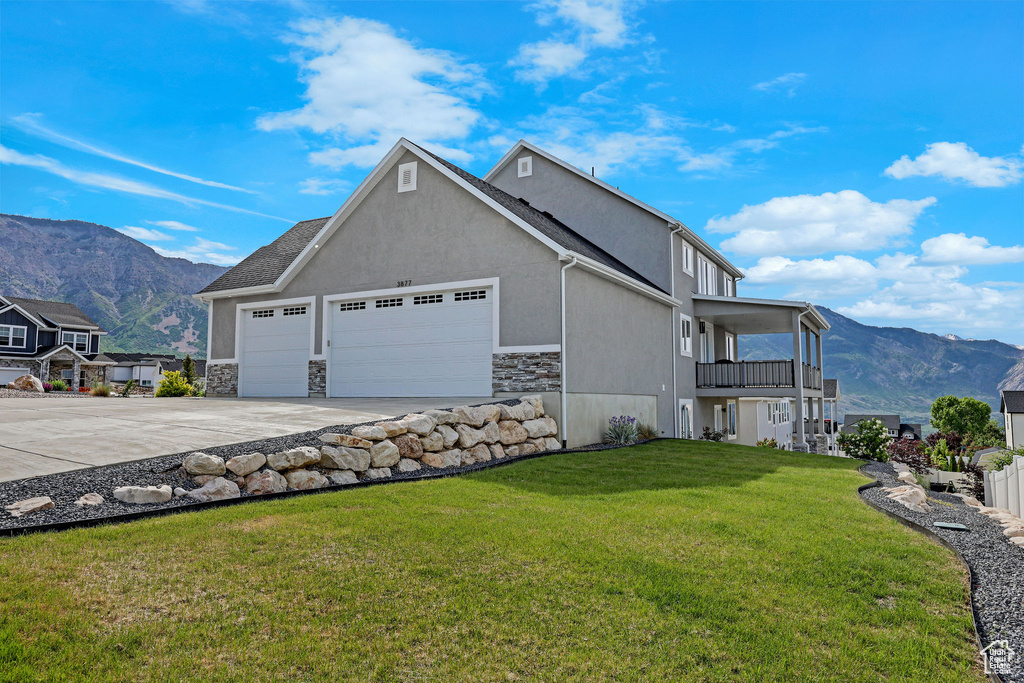 View of home\\\\\\\'s exterior featuring a garage, concrete driveway, a mountain view, a balcony, and a lawn