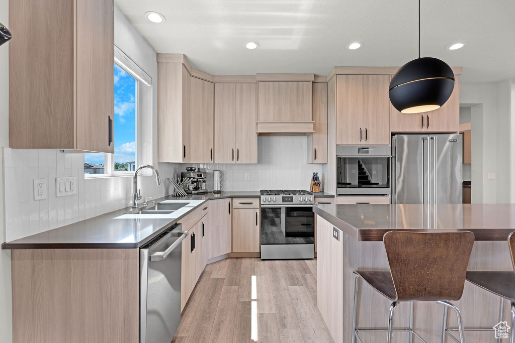 Kitchen with stainless steel appliances, a sink, light brown cabinets, a breakfast bar area, and light wood finished floors