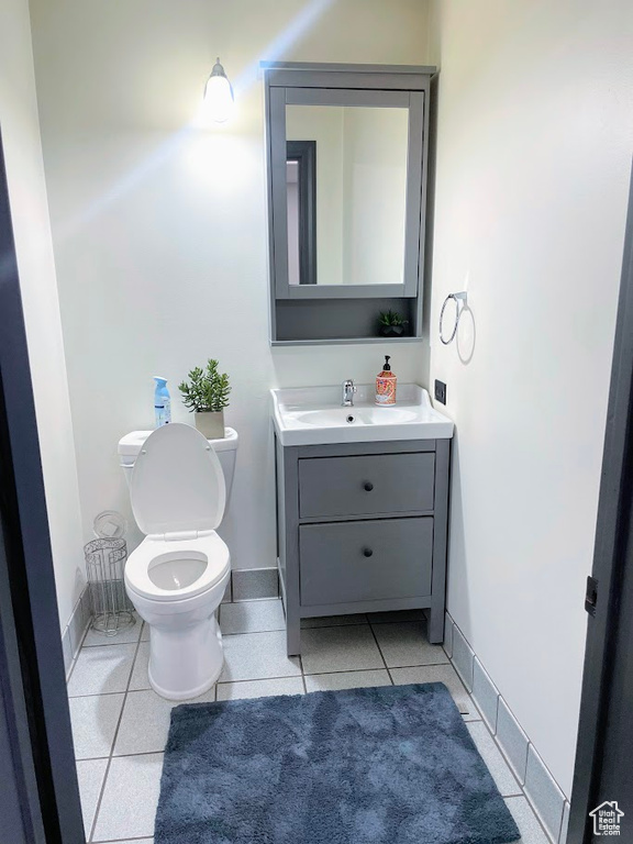 Half bathroom with vanity, toilet, baseboards, and tile patterned floors
