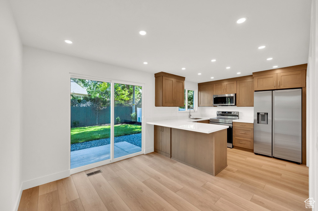 Kitchen with appliances with stainless steel finishes, a sink, a peninsula, light countertops, and light wood-type flooring