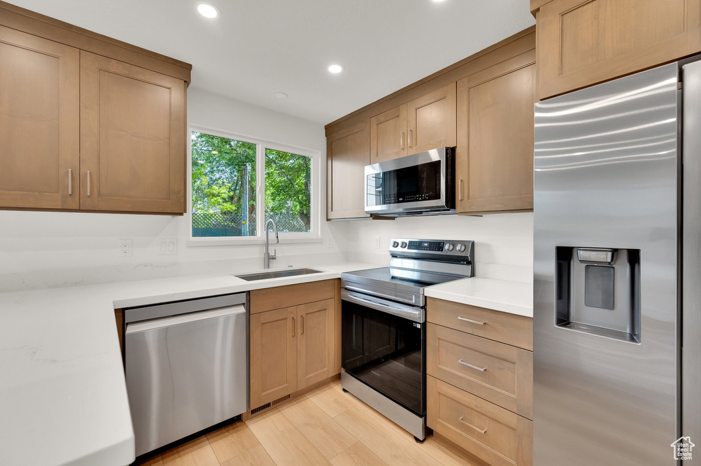 Kitchen with stainless steel appliances, a sink, light countertops, recessed lighting, and light wood finished floors