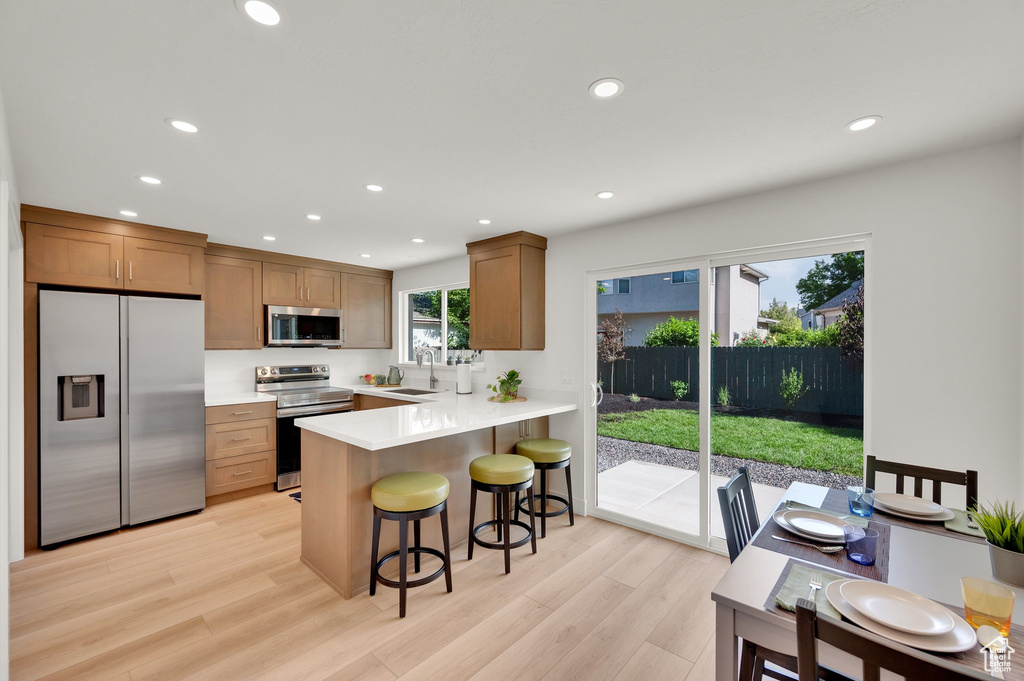 Kitchen with appliances with stainless steel finishes, a sink, recessed lighting, a breakfast bar area, and light wood-type flooring
