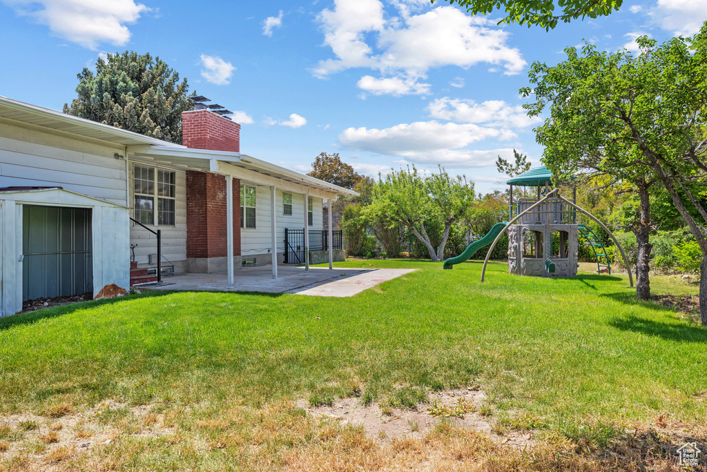 View of grassy yard featuring a playground and a patio area