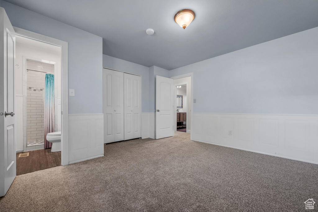 Unfurnished bedroom with a wainscoted wall, carpet, a closet, and ensuite bath