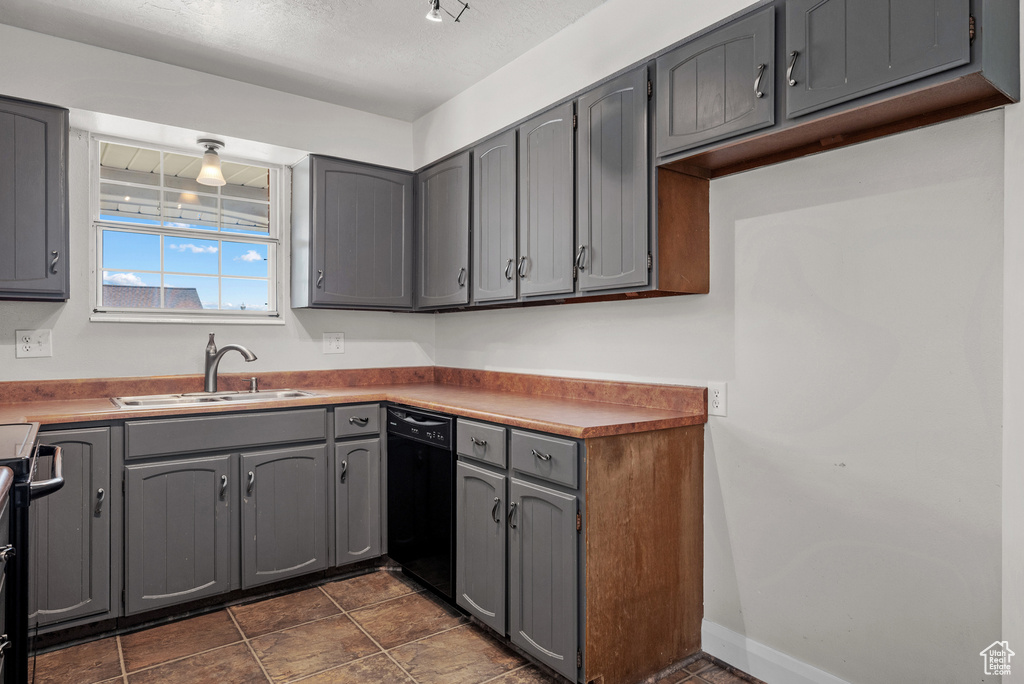 Kitchen featuring black dishwasher, a sink, gray cabinets, and baseboards