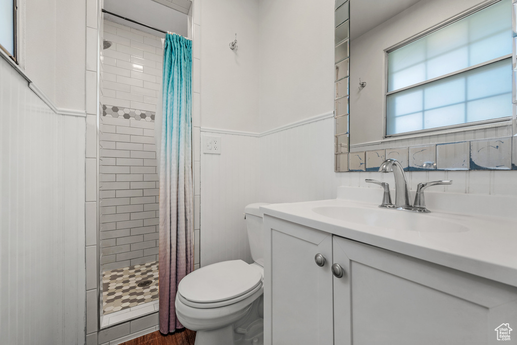 Bathroom featuring vanity, toilet, a tile shower, wainscoting, and wood finished floors
