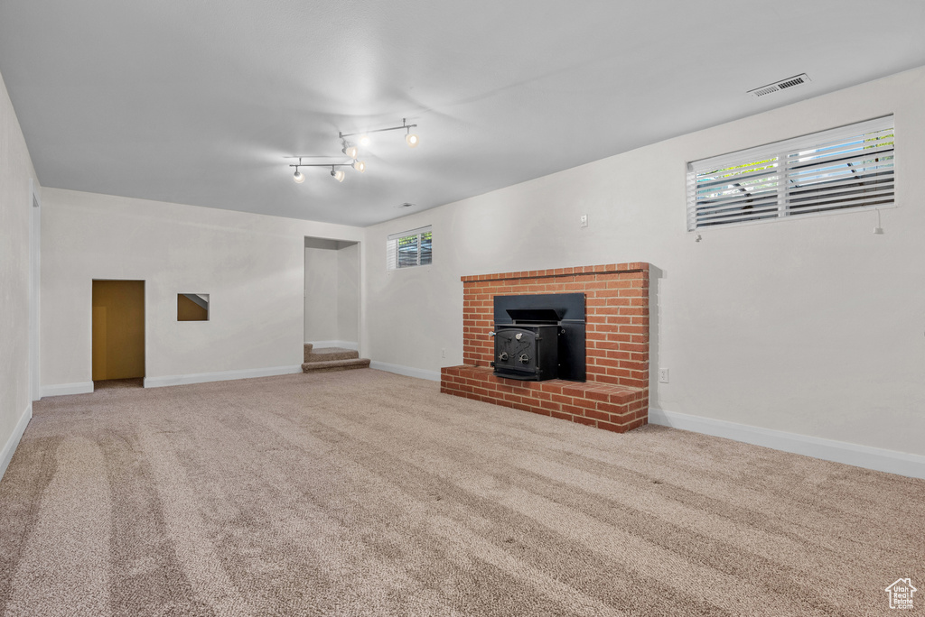 Unfurnished living room with a wood stove, carpet flooring, baseboards, and plenty of natural light