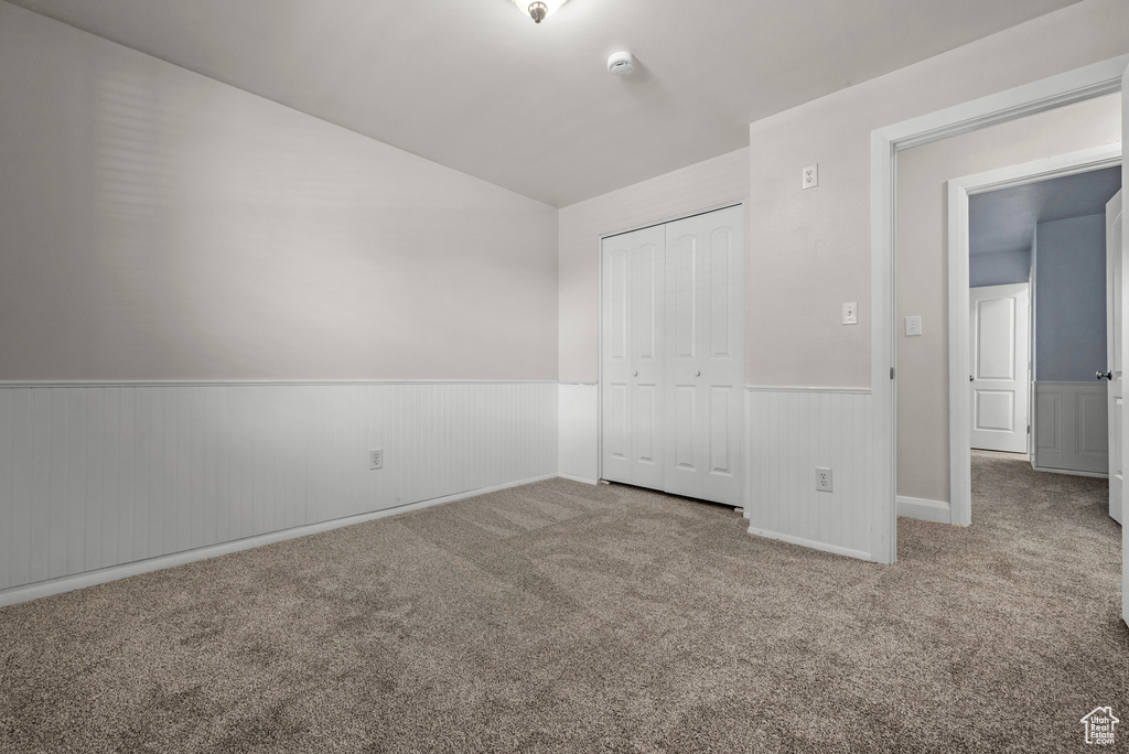 Unfurnished bedroom with a wainscoted wall, carpet flooring, a closet, and lofted ceiling