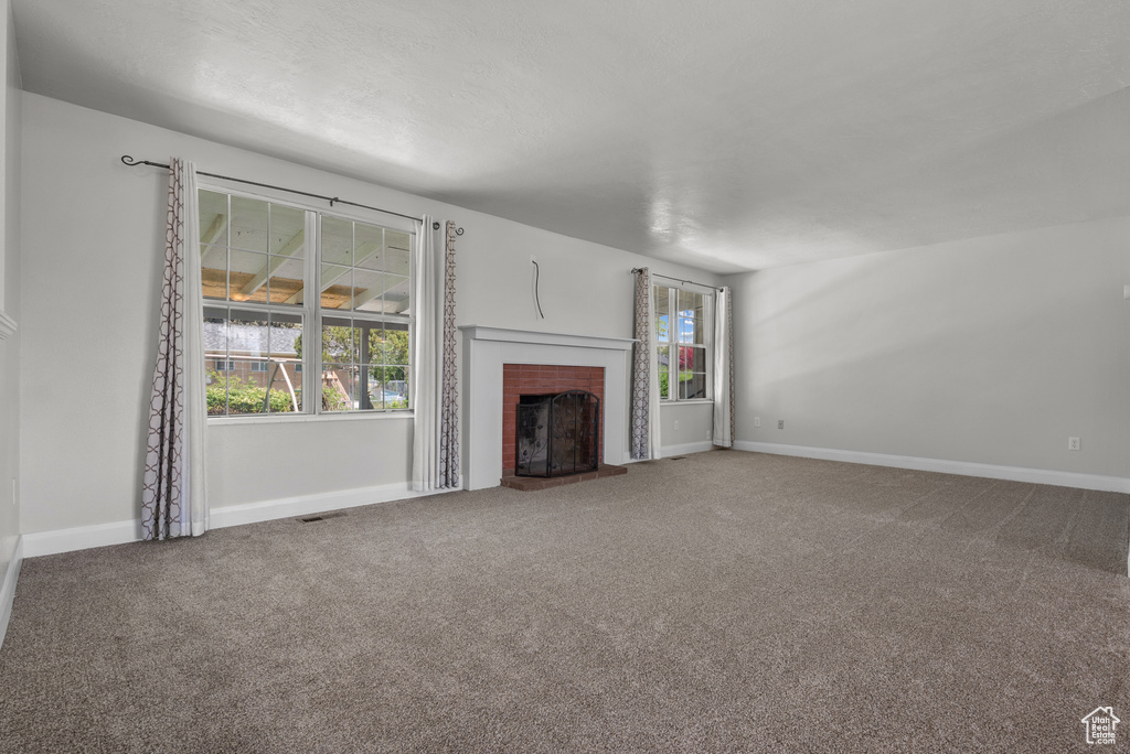 Unfurnished living room featuring plenty of natural light, carpet flooring, a brick fireplace, and baseboards