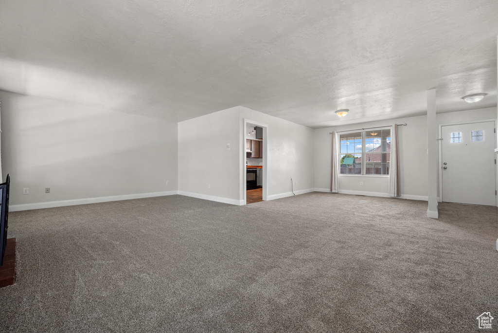 Unfurnished living room featuring carpet floors, baseboards, and a textured ceiling