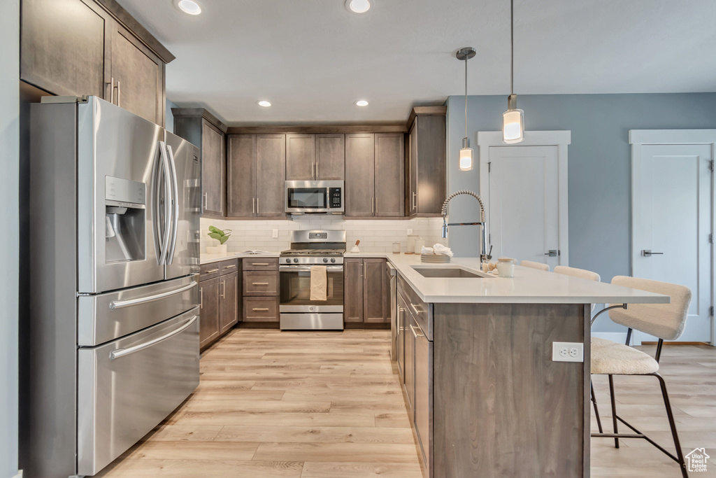Kitchen with appliances with stainless steel finishes, a peninsula, a sink, a breakfast bar area, and light wood-style floors