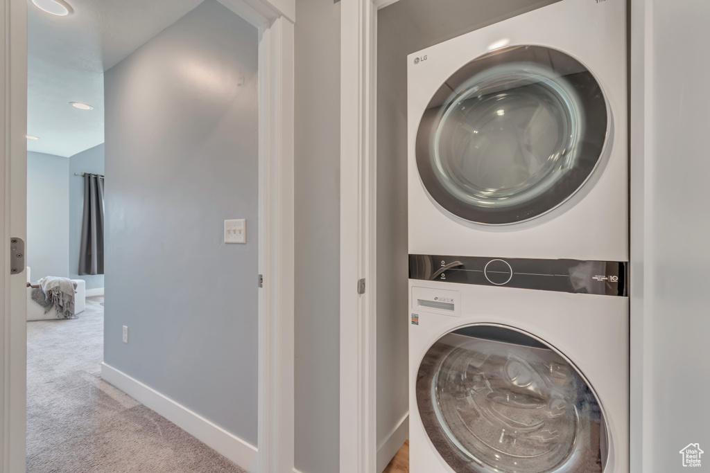 Washroom with stacked washer / dryer, light colored carpet, and baseboards