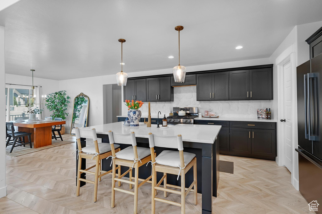 Kitchen with range, high quality fridge, light countertops, backsplash, and an island with sink