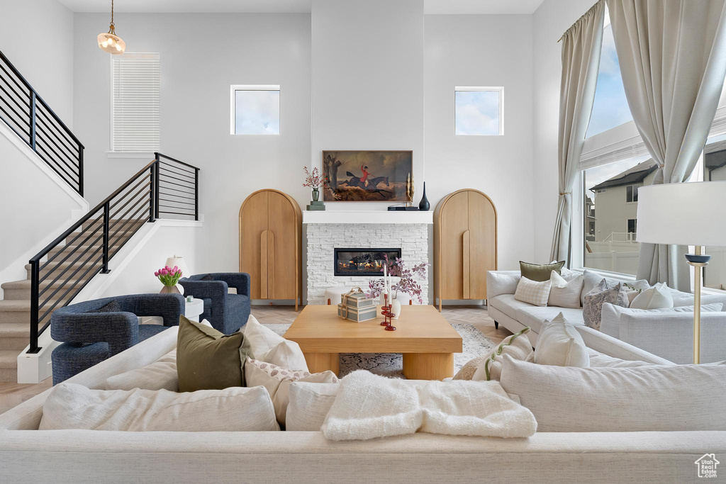 Living area with healthy amount of natural light, a towering ceiling, stairs, a stone fireplace, and wood finished floors