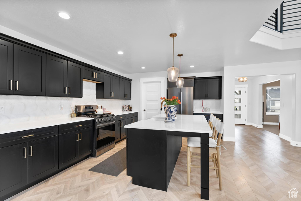 Kitchen with appliances with stainless steel finishes, dark cabinets, a breakfast bar, decorative backsplash, and recessed lighting