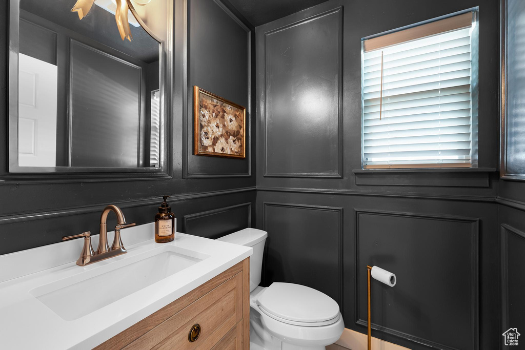 Half bathroom featuring toilet, a decorative wall, and vanity