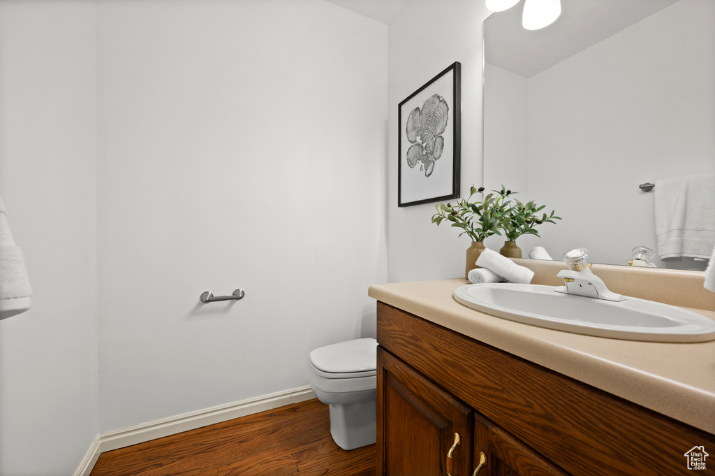 Half bathroom featuring vanity, toilet, wood finished floors, and baseboards