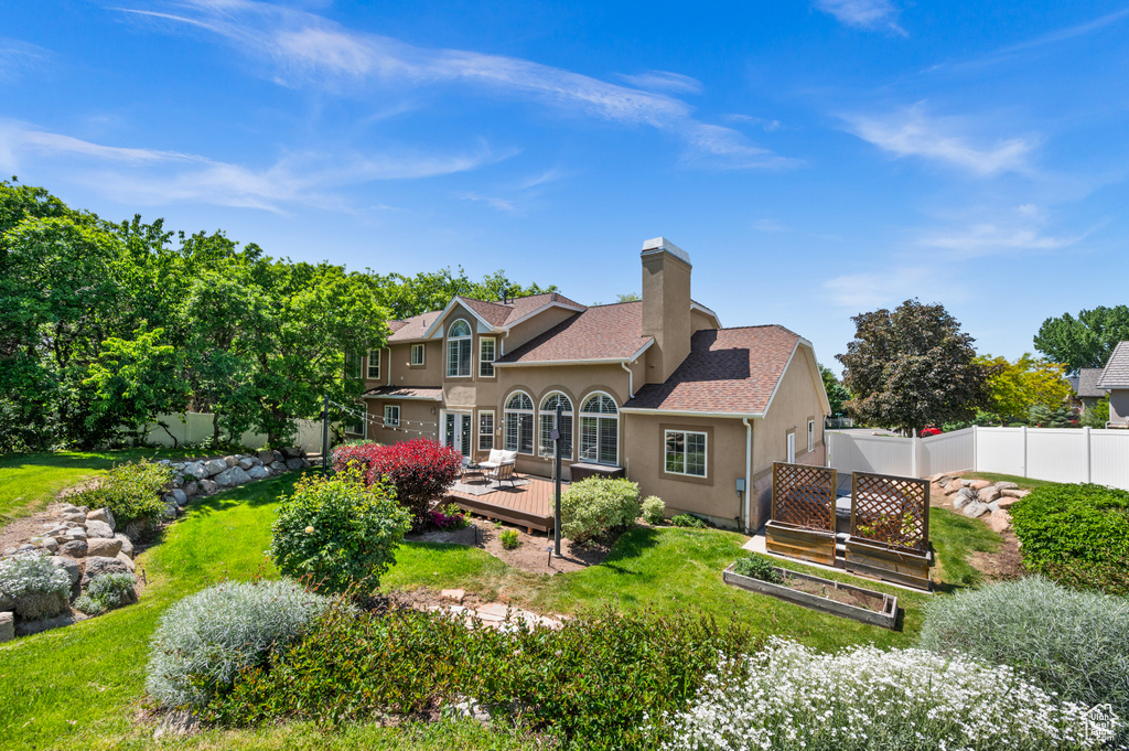 Rear view of house with stucco siding, a deck, a garden, a chimney, and a shingled roof