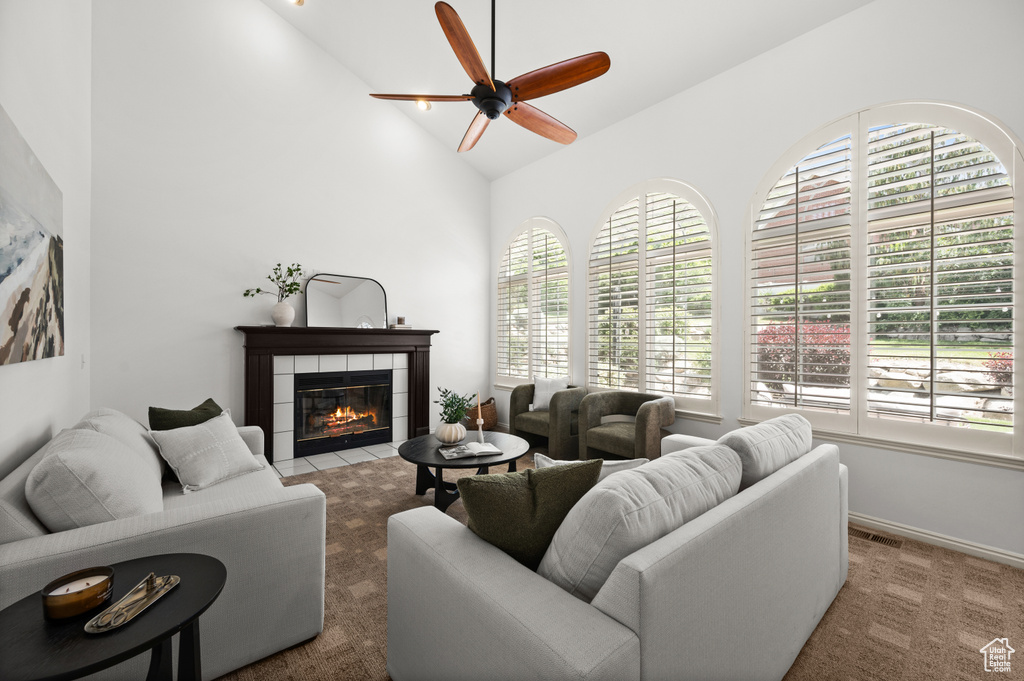 Carpeted living area with healthy amount of natural light, ceiling fan, a tiled fireplace, and high vaulted ceiling