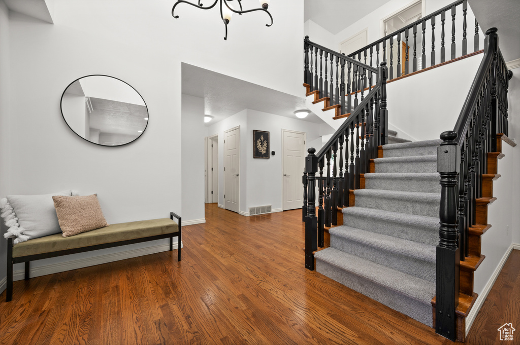 Stairs with baseboards, a towering ceiling, wood finished floors, and a chandelier