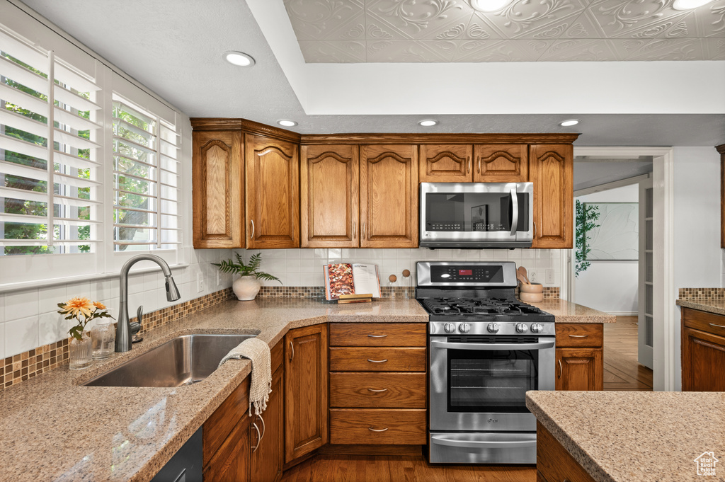 Kitchen featuring stainless steel appliances, a sink, tasteful backsplash, brown cabinets, and recessed lighting