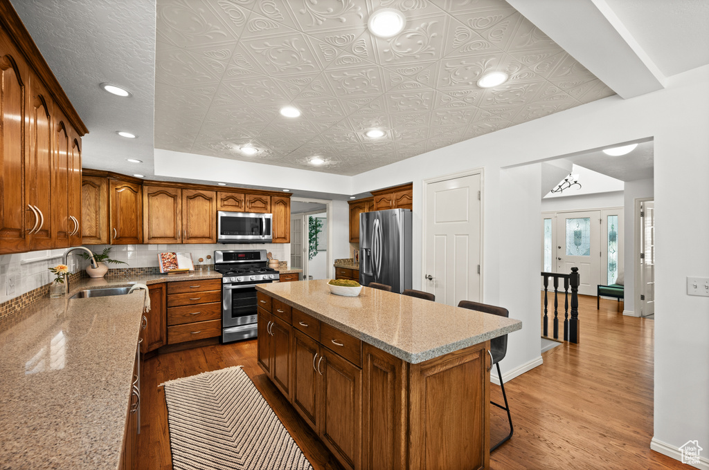 Kitchen featuring appliances with stainless steel finishes, a sink, a center island, wood finished floors, and recessed lighting