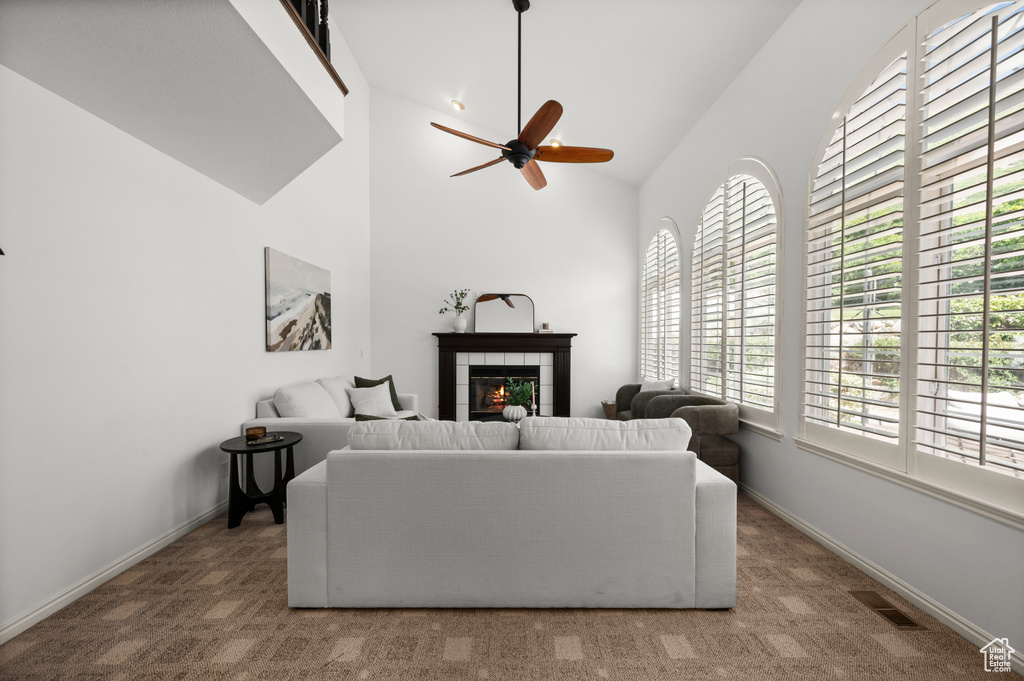 Living room featuring ceiling fan, a tiled fireplace, carpet floors, high vaulted ceiling, and baseboards