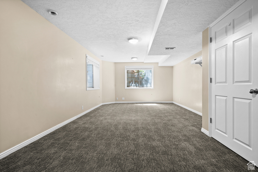 Empty room with dark colored carpet, a textured ceiling, and baseboards