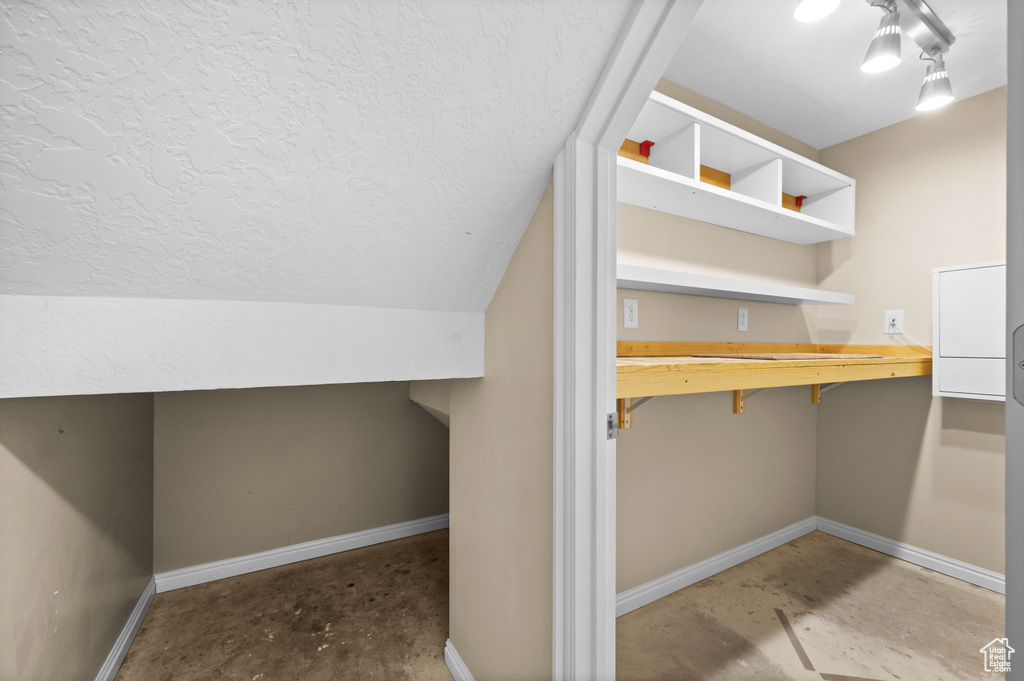Bonus room featuring concrete floors, baseboards, a textured ceiling, lofted ceiling, and a desk