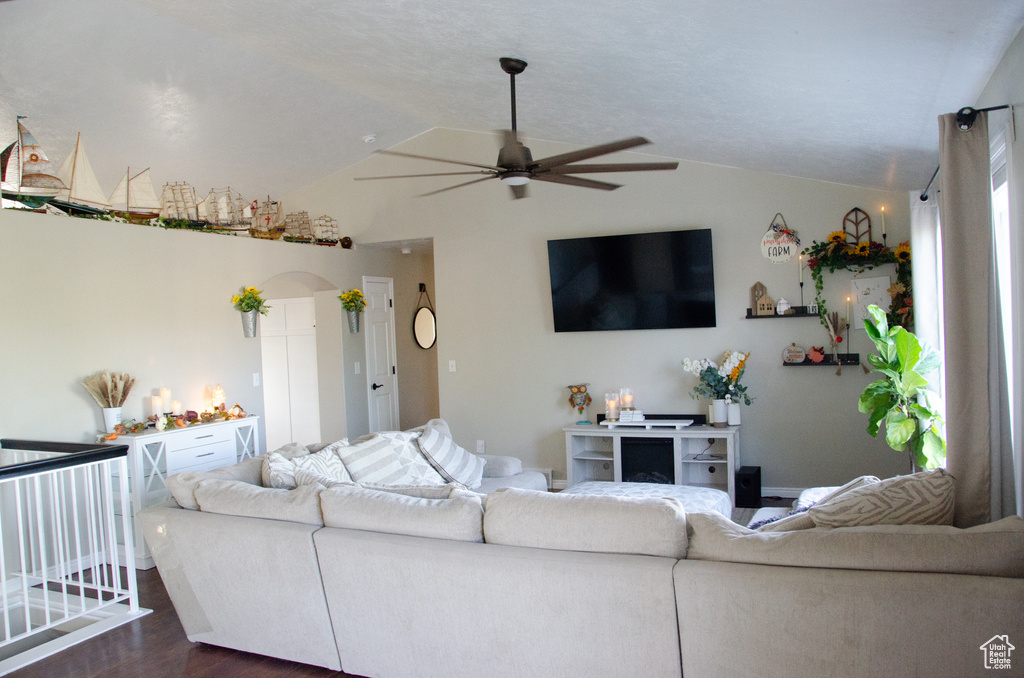 Living area featuring ceiling fan, vaulted ceiling, dark wood-type flooring, and arched walkways