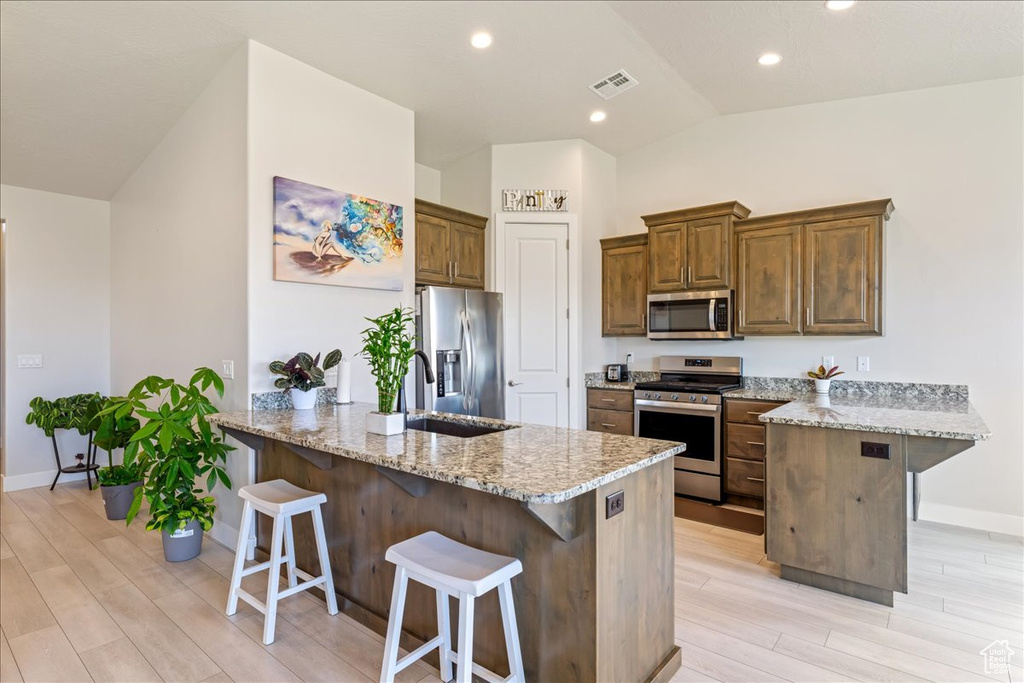 Kitchen with appliances with stainless steel finishes, a peninsula, vaulted ceiling, a breakfast bar, and light wood finished floors