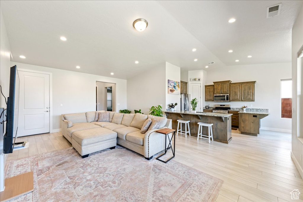 Living area featuring light wood-type flooring, vaulted ceiling, baseboards, and recessed lighting