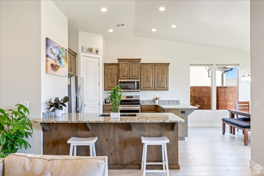 Kitchen with stainless steel appliances, vaulted ceiling, a peninsula, a kitchen bar, and light stone countertops