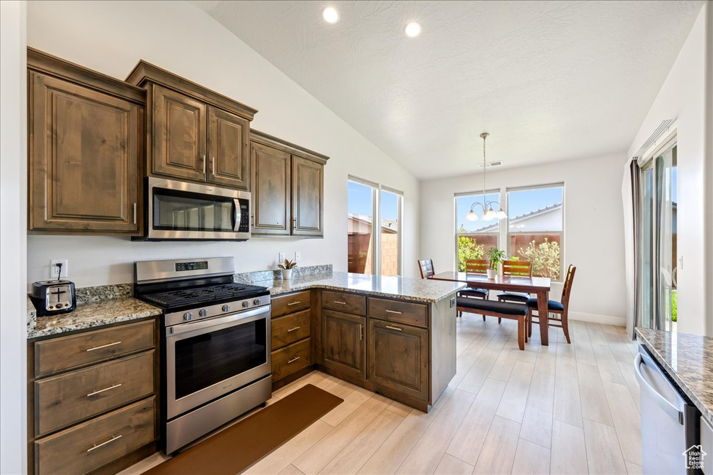 Kitchen featuring appliances with stainless steel finishes, light stone countertops, light wood-type flooring, a peninsula, and pendant lighting
