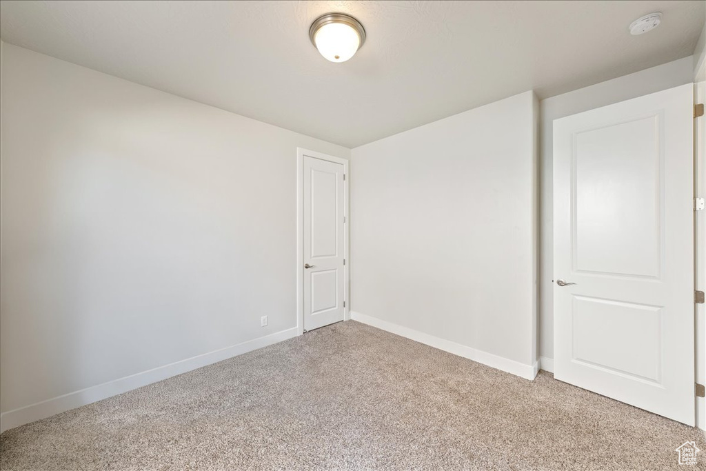 Unfurnished room featuring light carpet, baseboards, and a smoke detector
