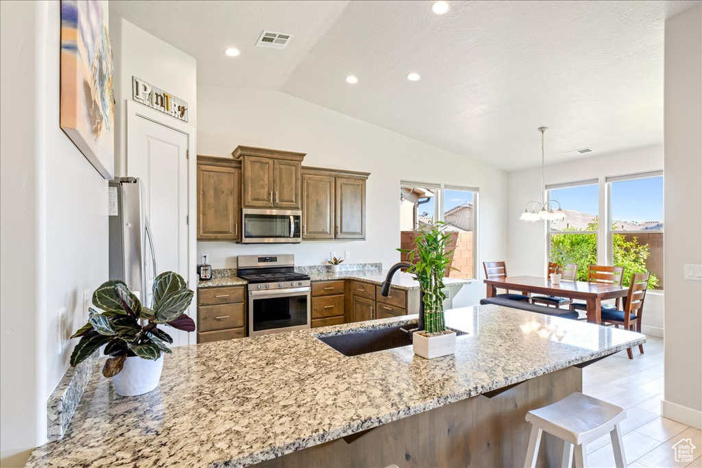 Kitchen with stainless steel appliances, a sink, a peninsula, lofted ceiling, and brown cabinets