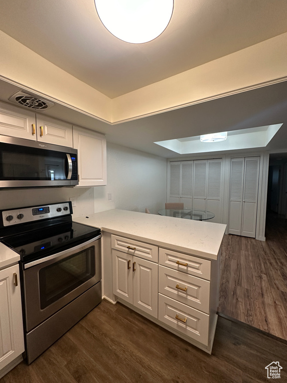 Kitchen featuring appliances with stainless steel finishes, dark wood-style flooring, white cabinetry, and a peninsula