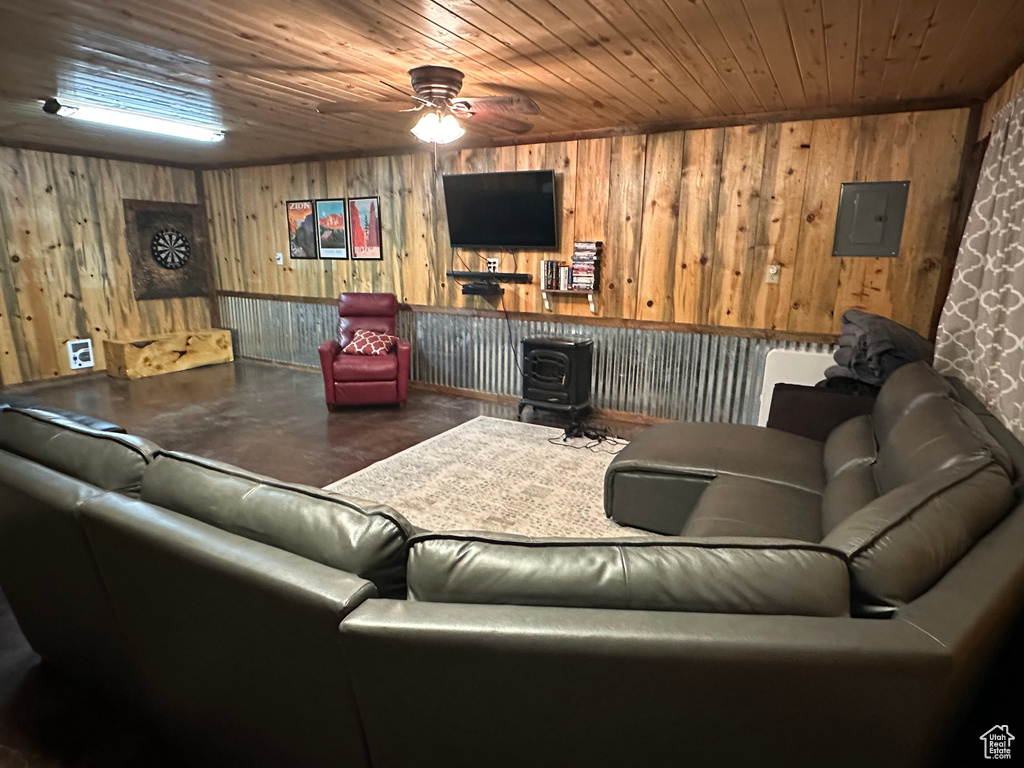 Living area with a wood stove, wood ceiling, a ceiling fan, electric panel, and concrete flooring