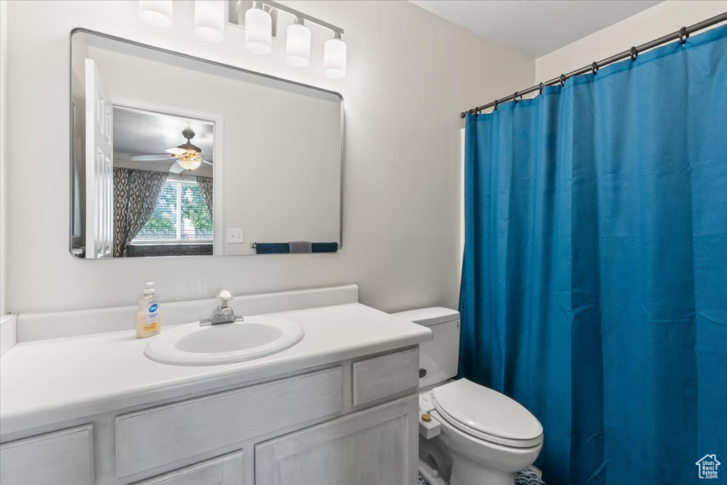 Full bath with toilet, vanity, ceiling fan, and a shower with curtain