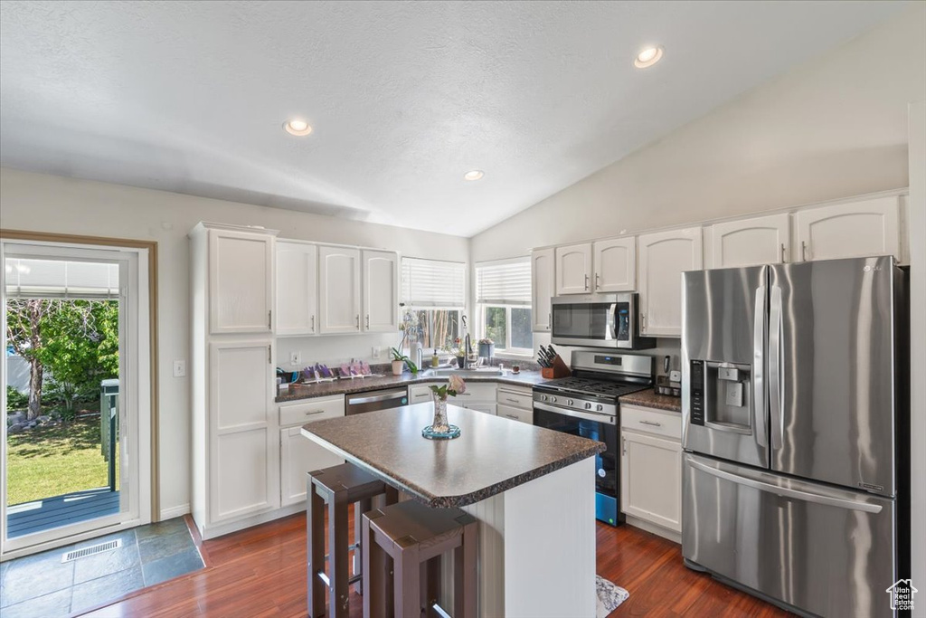 Kitchen with appliances with stainless steel finishes, vaulted ceiling, dark countertops, white cabinetry, and dark wood finished floors
