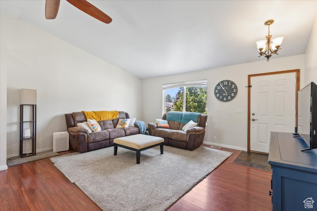 Living room featuring vaulted ceiling, dark wood-style floors, a chandelier, a ceiling fan, and baseboards