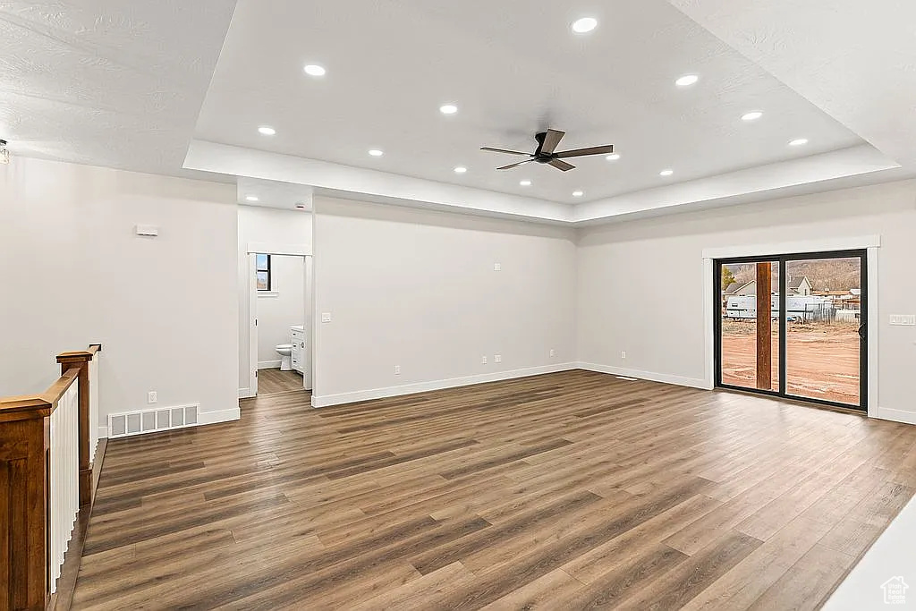 Empty room with a tray ceiling, wood finished floors, ceiling fan, baseboards, and recessed lighting