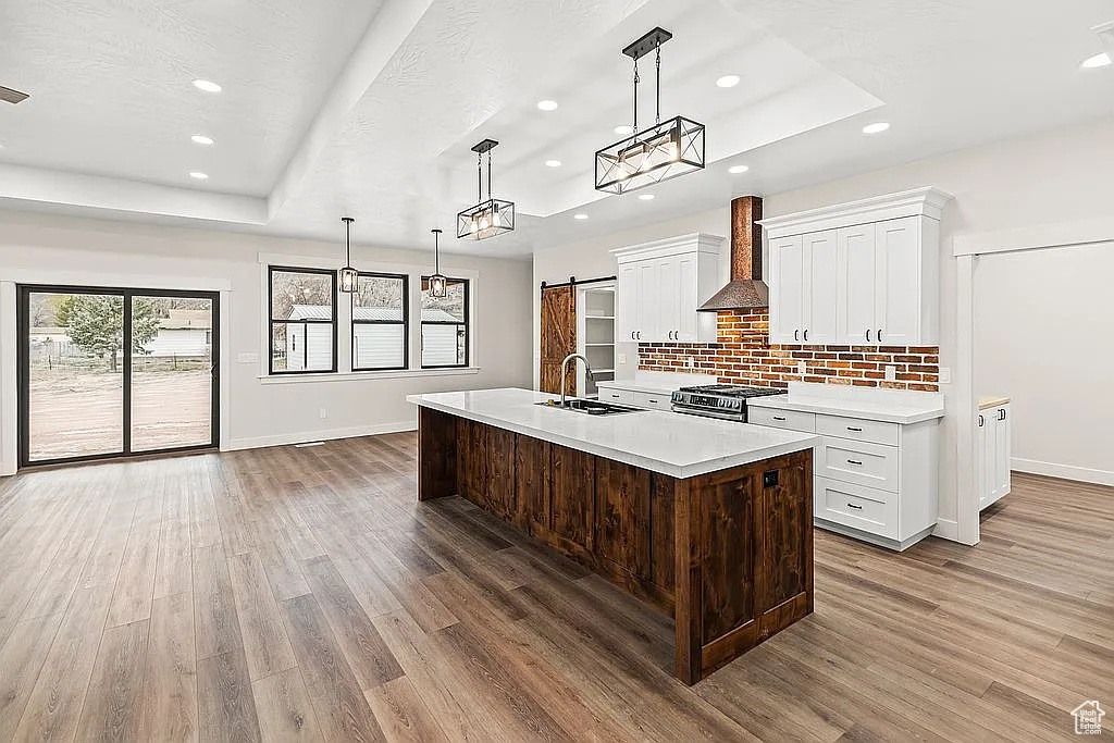 Kitchen featuring a raised ceiling, wall chimney range hood, light countertops, baseboards, and stainless steel gas stove