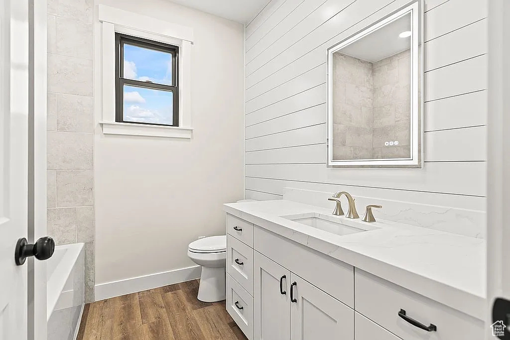 Bathroom with vanity, toilet, wood finished floors, baseboards, and wood walls