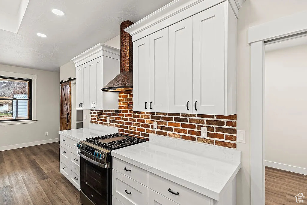 Kitchen with stainless steel gas stove, a barn door, baseboards, wall chimney range hood, and decorative backsplash