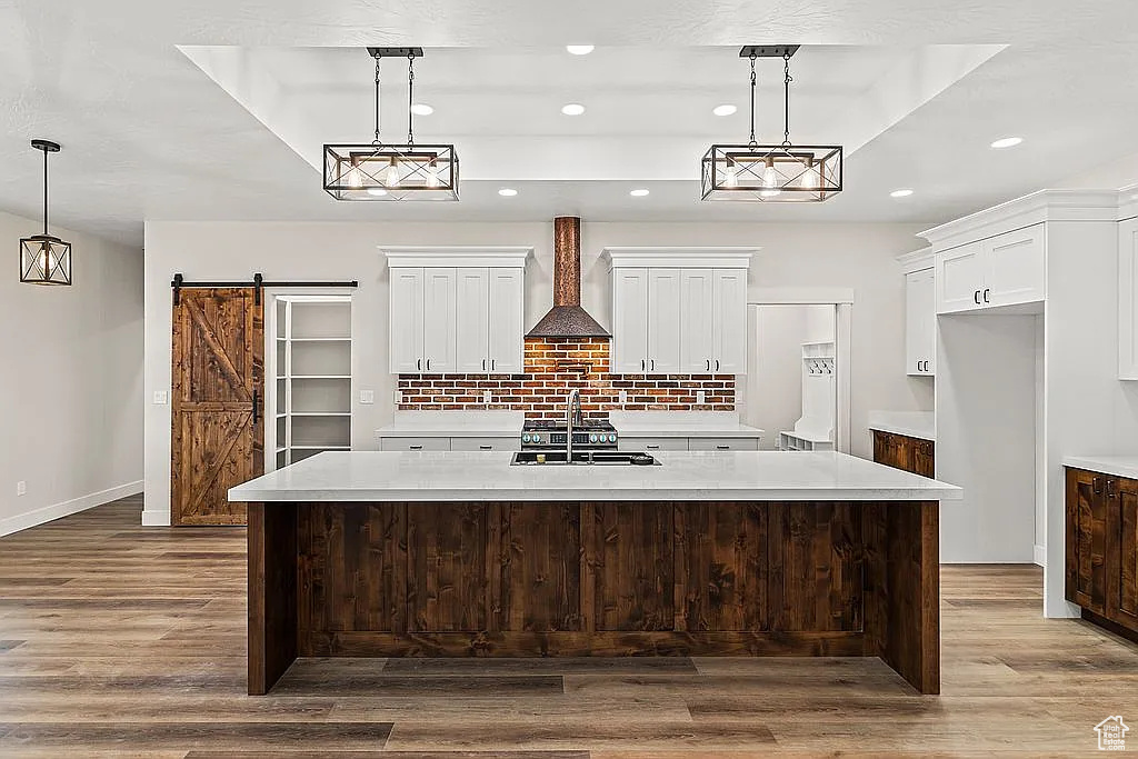 Kitchen featuring a sink, wall chimney exhaust hood, dark wood-style flooring, tasteful backsplash, and light countertops