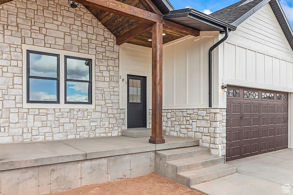 Entrance to property featuring stone siding, board and batten siding, a garage, and driveway