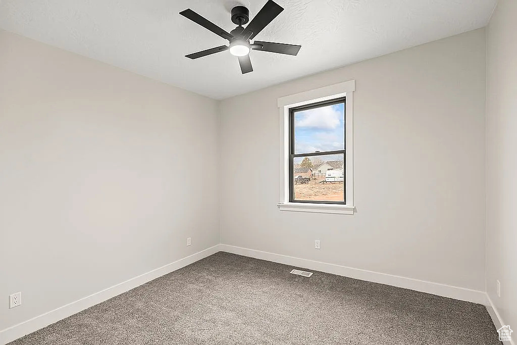 Carpeted empty room featuring a ceiling fan and baseboards
