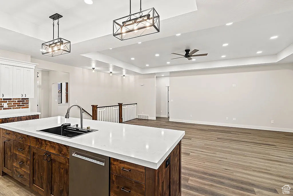 Kitchen with a sink, a raised ceiling, light wood-style flooring, dishwasher, and light countertops