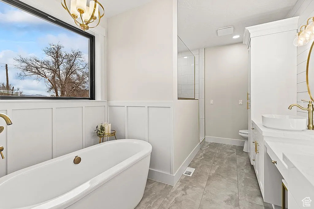Bathroom featuring a soaking tub, marble look tiles, vanity, toilet, and a decorative wall